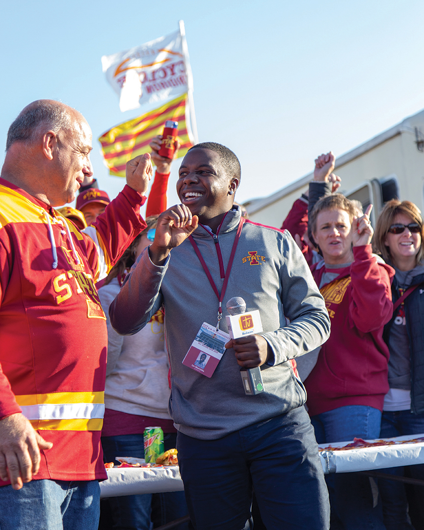 Lester MMwirichia stands in a crowd with a microphone at an Iowa State tailgate.