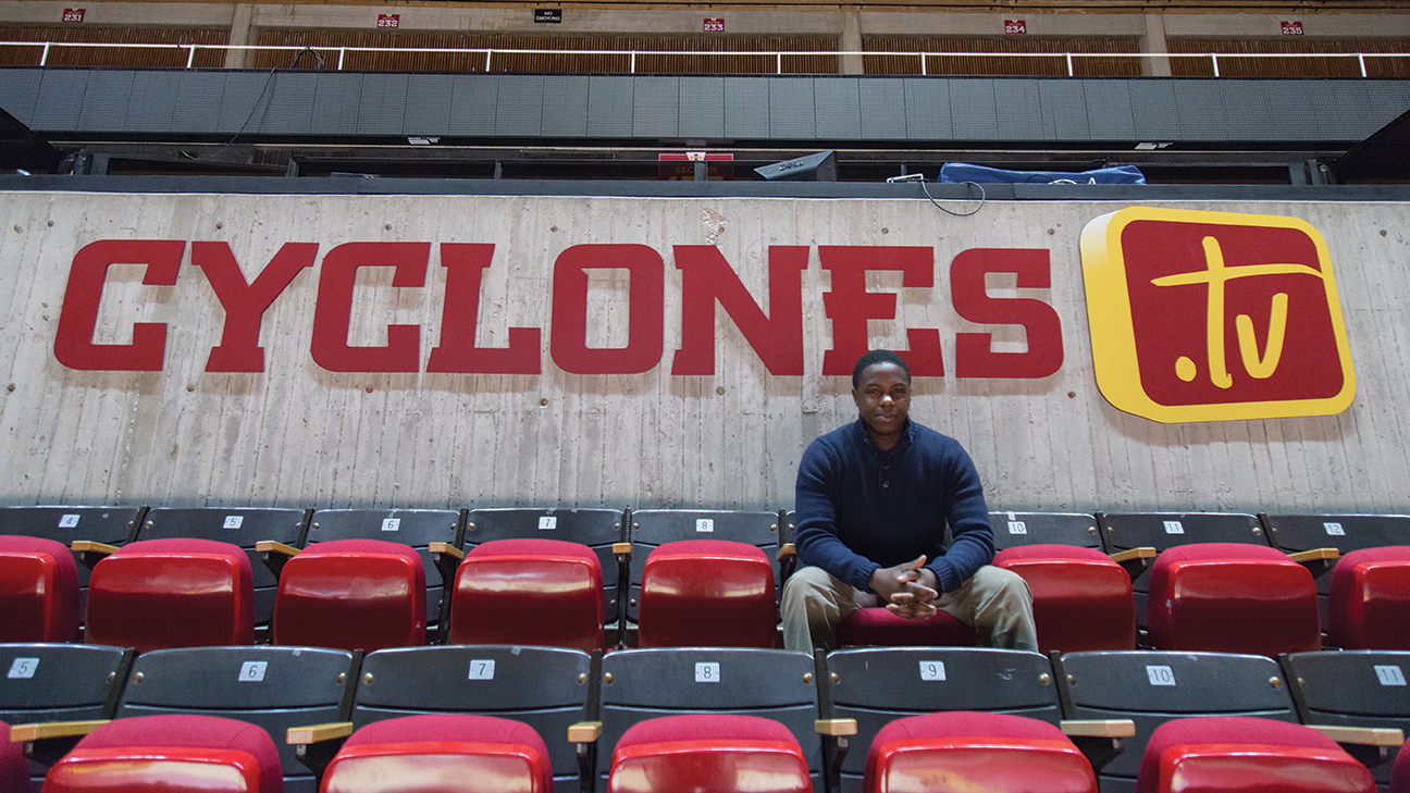 Lester Mwirichia sits in the stands at Hilton Coliseum in front of the Cyclones.TV sign.
