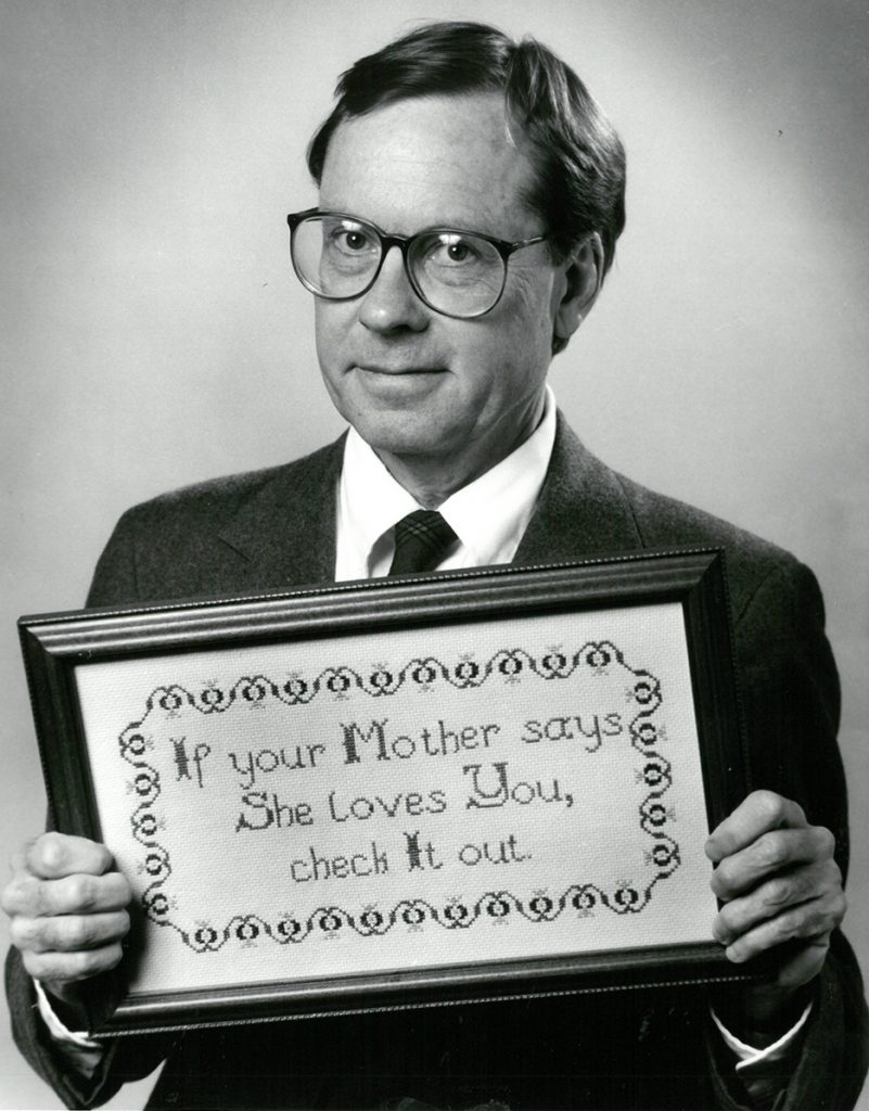 Giles Fowler with cross-stitch saying, "If your Mother says she loves you, check it out."